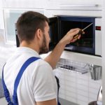 Young,man,repairing,microwave,oven,in,kitchen