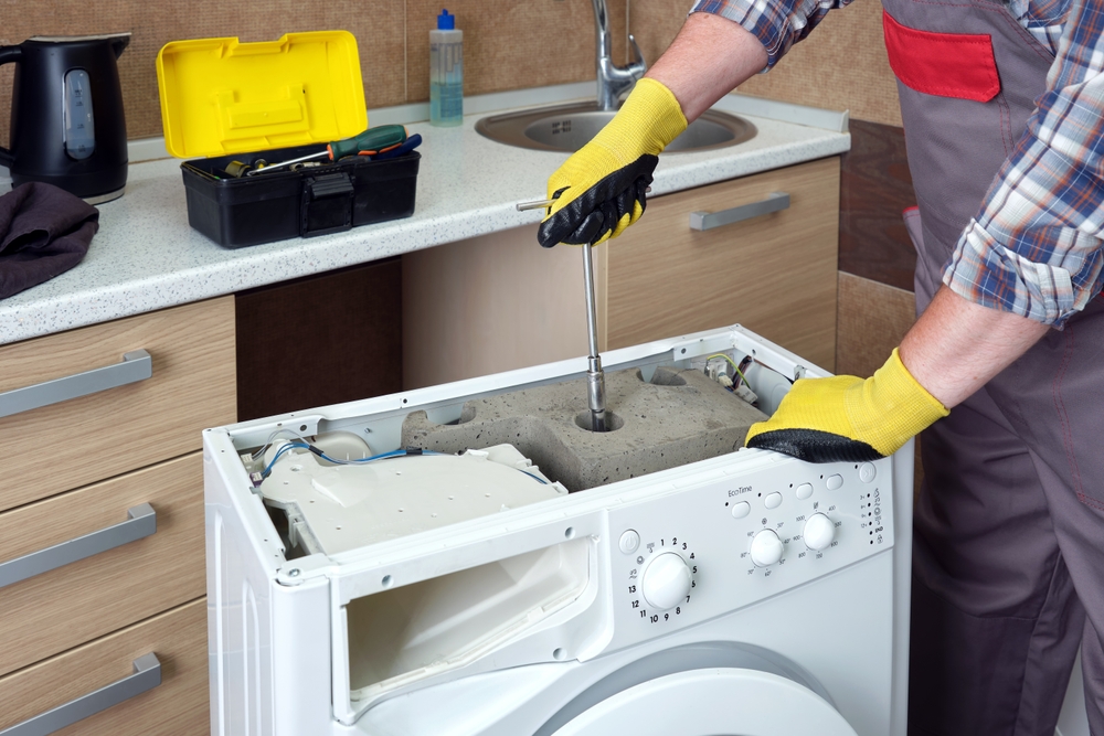 A,service,technician,repairs,a,household,washing,machine.,against,the