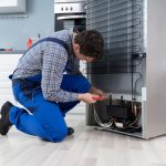 Male,worker,repairing,refrigerator,with,screwdriver,in,house