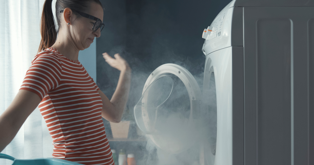 Upset,woman,staring,at,her,broken,washing,machine,,the,room